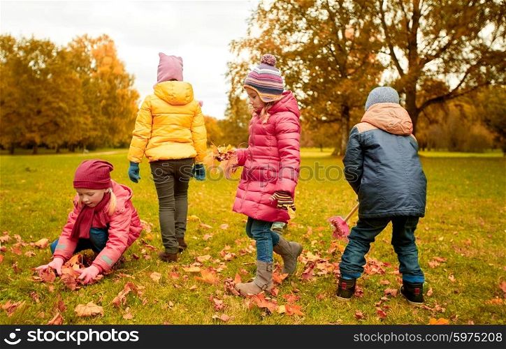 childhood, leisure, autumn, friendship and people concept - group of children with rack collecting and racking leaves in park