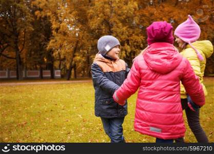 childhood, leisure, friendship and people concept - group of happy children holding hands and playing in autumn park