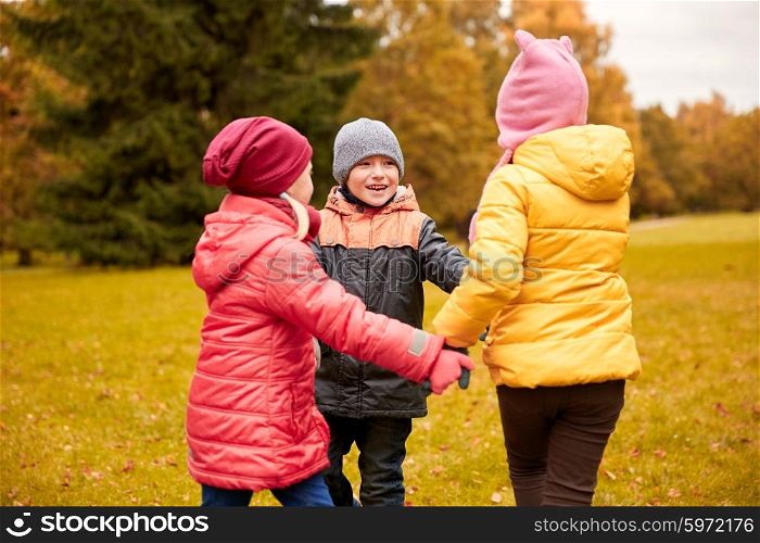 childhood, leisure, friendship and people concept - group of happy children holding hands and playing in autumn park