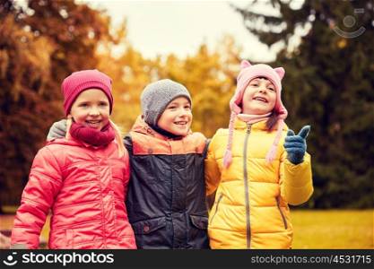 childhood, leisure, friendship and people concept - group of happy kids hugging and pointing finger to something in autumn park