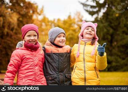childhood, leisure, friendship and people concept - group of happy kids hugging and pointing finger to something in autumn park