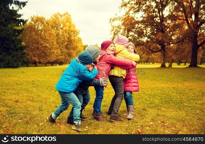 childhood, leisure, friendship and people concept - group of happy kids hugging in autumn park
