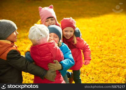 childhood, leisure, friendship and people concept - group of happy kids hugging in autumn park