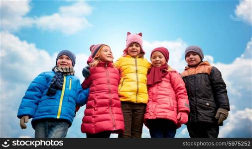 childhood, leisure, friendship and people concept - group of happy kids hugging over blue sky background