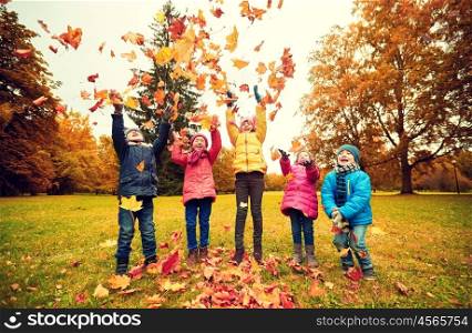 childhood, leisure, friendship and people concept - group of happy kids playing with autumn maple leaves and having fun in park