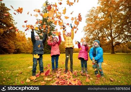 childhood, leisure, friendship and people concept - group of happy kids playing with autumn maple leaves and having fun in park