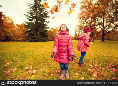 childhood, leisure, friendship and people concept - group of happy little girl playing with autumn maple leaves and having fun in park