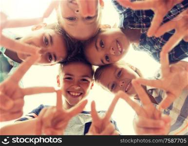 childhood, leisure, friendship and people concept - group of smiling happy children showing v sign in circle. group of happy children showing v sign in circle