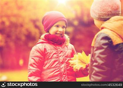 childhood, leisure, friendship and people concept - happy little boy giving maple leaves to girl in autumn park