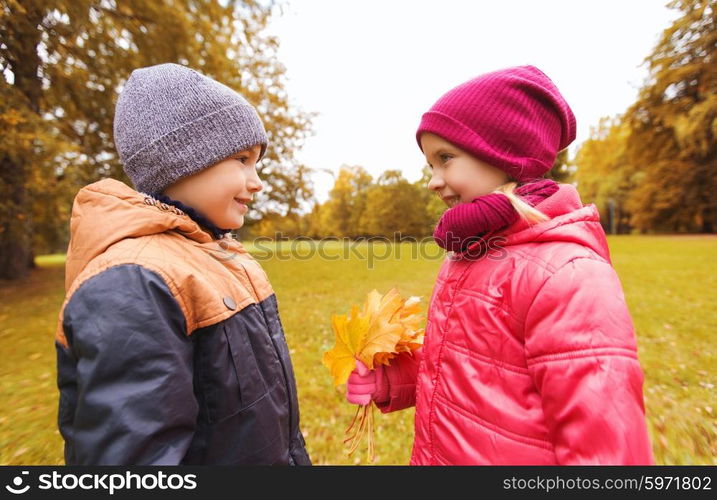 childhood, leisure, friendship and people concept - happy little boy giving maple leaves to girl in autumn park