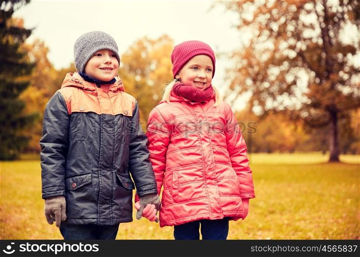 childhood, leisure, friendship and people concept - happy little girl and boy holding hands in autumn park