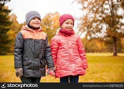 childhood, leisure, friendship and people concept - happy little girl and boy holding hands in autumn park