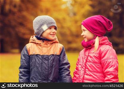 childhood, leisure, friendship and people concept - happy little girl and boy talking in autumn park