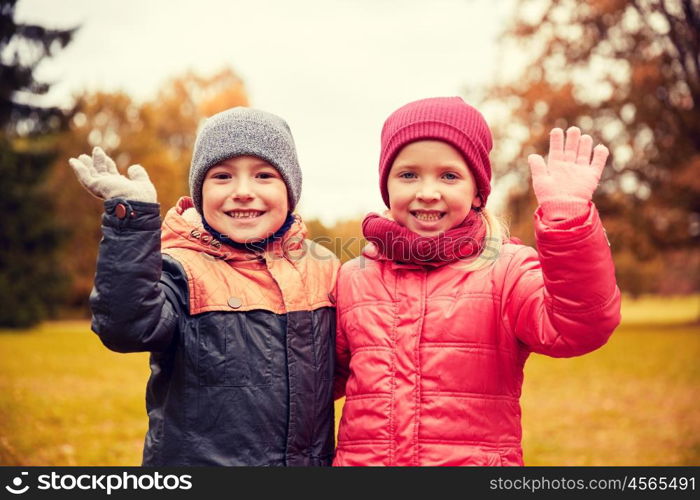 childhood, leisure, friendship, autumn and people concept - happy little girl and boy waving hands in park