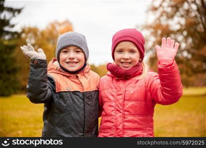 childhood, leisure, friendship, autumn and people concept - happy little girl and boy waving hands in park