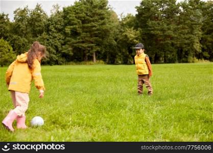 childhood, leisure games and people concept - happy little boy and girl with ball playing soccer at summer park. little children with ball playing soccer at park