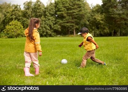 childhood, leisure games and people concept - happy little boy and girl with ball playing soccer at summer park. little children with ball playing soccer at park