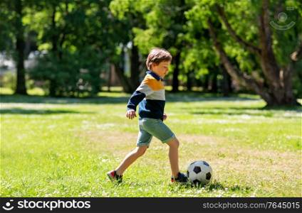 childhood, leisure games and people concept - happy little boy with ball playing soccer at summer park. happy little boy with ball playing soccer at park