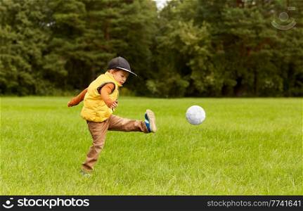 childhood, leisure games and people concept - happy little boy with ball playing soccer at summer park. little boy with ball playing soccer at park