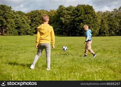 childhood, leisure games and people concept - happy little boys with ball playing soccer at summer park. happy little boys with ball playing soccer at park