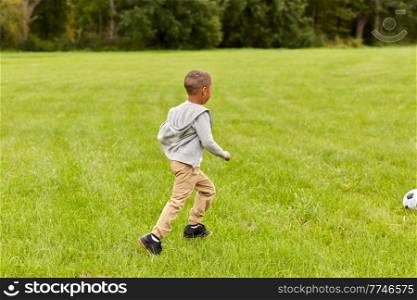 childhood, leisure games and people concept - little boy with ball playing soccer at summer park. little boy with ball playing soccer at park