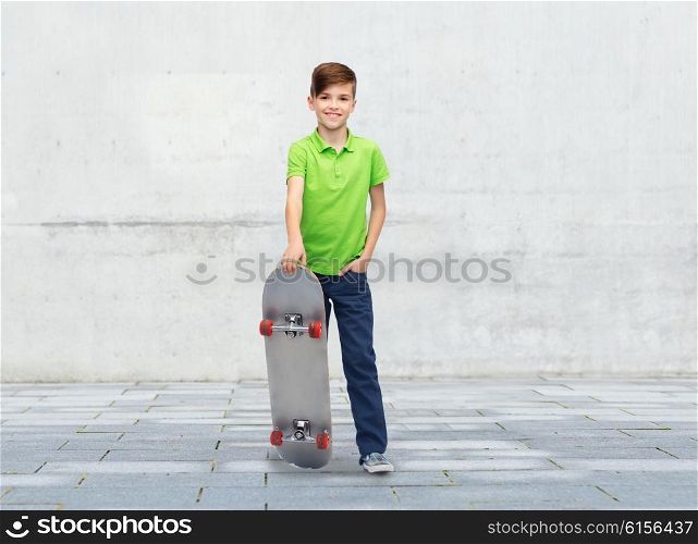 childhood, leisure, school and people concept - happy smiling boy with skateboard over concrete gray wall on city street background