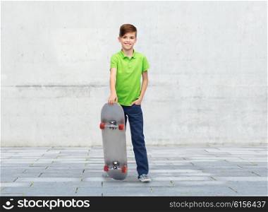 childhood, leisure, school and people concept - happy smiling boy with skateboard over concrete gray wall on city street background