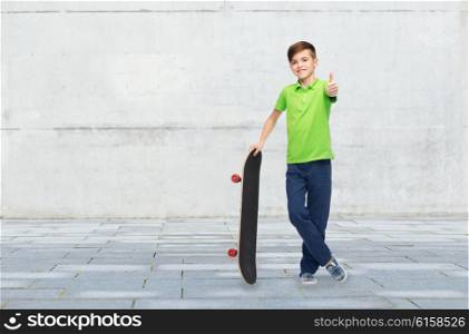 childhood, leisure, school and people concept - happy smiling boy with skateboard showing thumbs up over concrete gray wall on city street background