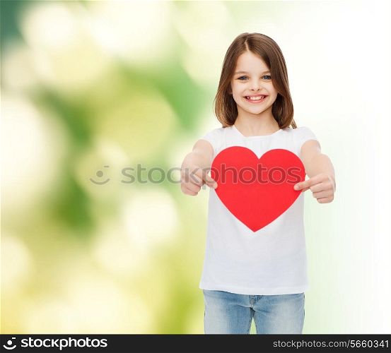 childhood, love, charity, ecology and people concept - smiling little girl sitting and holding red heart cutout over green background