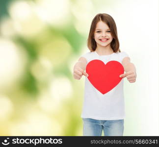 childhood, love, charity, ecology and people concept - smiling little girl sitting and holding red heart cutout over green background