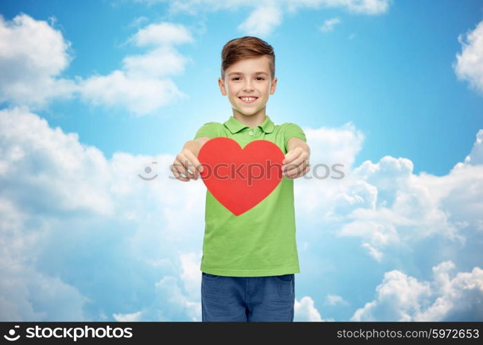 childhood, love, charity, health care and people concept - happy smiling boy in green polo t-shirt holding blank red heart shape over blue sky and clouds background