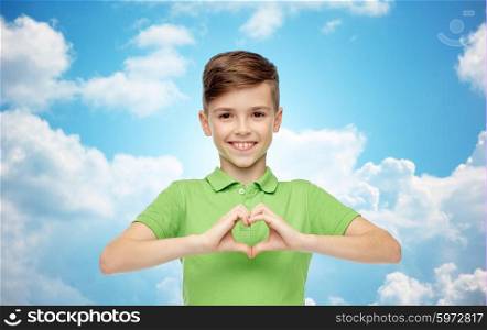 childhood, love, charity, health care and people concept - happy smiling boy in green polo t-shirt showing heart hand sign over blue sky and clouds background