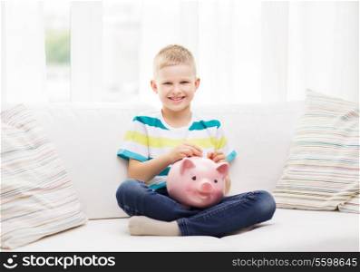childhood, money, investment and happy people concept - smiling little boy with piggy bank and money at home