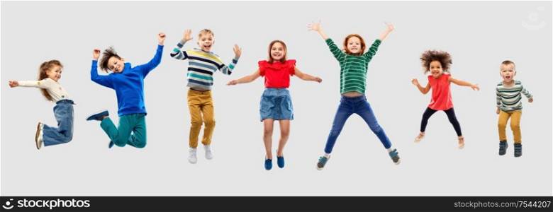 childhood, motion and happiness concept - happy little children jumping in air over grey background. happy children jumping in air over grey background