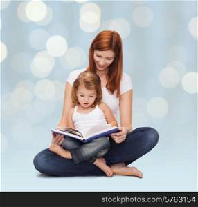 childhood, parenting and literature concept - happy mother with adorable little girl reading book over holidays lights background