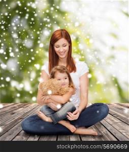 childhood, parenting and people concept - happy mother with little girl and teddy bear toy over wooden floor and green plants background