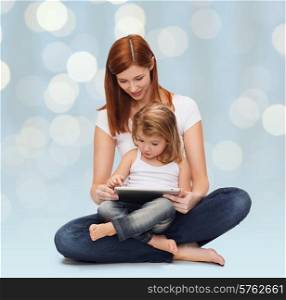 childhood, parenting and technology concept - happy mother with adorable little girl and tablet pc computer over holidays lights background