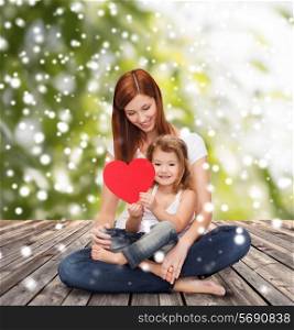 childhood, parenting, love and people concept - happy mother with little girl and red heart over wooden floor and green plants background