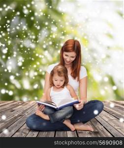 childhood, parenting, people and education concept - happy mother with little girl reading book over wooden floor and green plants background