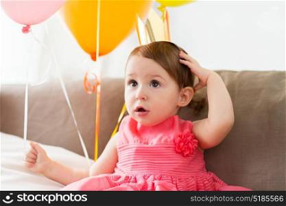 childhood, people and celebration concept - happy baby girl wearing crown on birthday party at home. happy baby girl in crown on birthday party at home