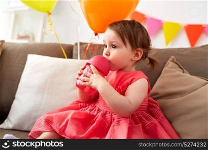 childhood, people and holidays concept - baby girl drinking from sippy cup or bottle at home birthday party. baby girl drinking from sippy cup at birthday