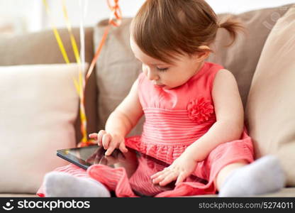 childhood, people and technology concept - happy baby girl with tablet pc computer sitting on sofa at home. baby girl with tablet pc sitting on sofa at home