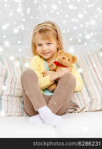 childhood, people, holidays and happiness concept - smiling little girl with teddy bear sitting on sofa at home