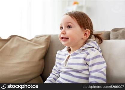 childhood, portrait and people concept - happy smiling baby girl sitting on sofa at home. happy smiling baby girl sitting on sofa at home