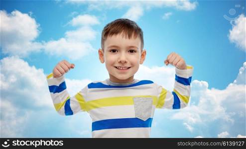 childhood, power, gesture and people concept - happy smiling little boy with raised hand over blue sky and clouds background
