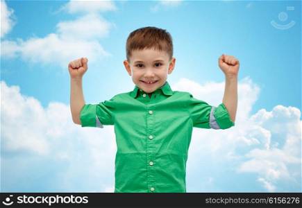 childhood, power, gesture and people concept - happy smiling little boy with raised hands showing his power over blue sky and clouds background