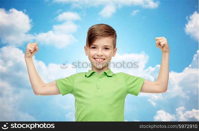 childhood, power, strength and people concept - happy smiling boy in green polo t-shirt showing strong fists over blue sky and clouds background