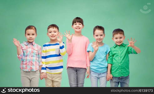 childhood, preschool education, friendship and people concept - group of happy smiling little children holding hands over green school chalk board background