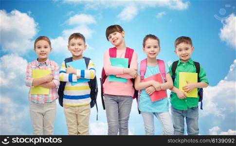 childhood, preschool education, learning and people concept - group of happy smiling little children with school bags and notebooks over blue sky and clouds background