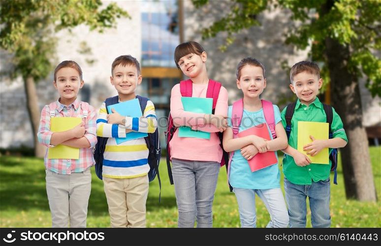 childhood, preschool education, learning and people concept - group of happy smiling little children with school bags and notebooks over summer campus background